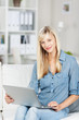 blonde frau sitzt mit laptop auf dem sofa