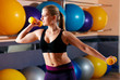 sports blonde woman performs exercises with dumbbells in the gym