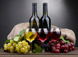 bottles and glasses of wine and grapes on grey background