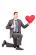 A smiling male in a suit kneeling with red heart