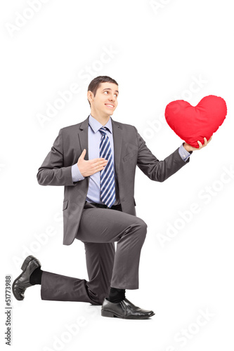 Photo: A smiling male in a suit kneeling with red heart A smiling male in a suit kneeling with red heart