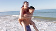 Man Giving Woman Piggyback As They Run Along Beach
