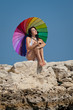 Attractive brunette with iridescent umbrella on wild rocky beach