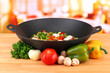 Wok with vegetable ragout on wooden table, on bright background
