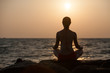 Silhouette of woman that meditates at the sea during sunset
