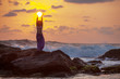Woman stands at the rock and takes sunset sun in her hands