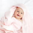 Caucasian baby boy covered with pink towel joyfully smiles at ca