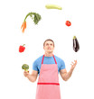 Young handsome male wearing apron and juggling with vegetables
