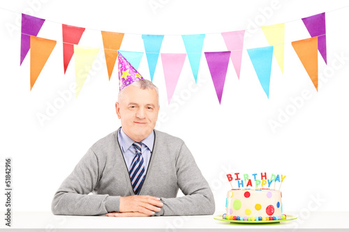 Photo: Happy mature gentleman with party hat and a birthday cake Happy mature gentleman with party hat and a birthday cake