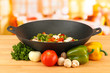 Wok with vegetable ragout on wooden table, on bright background