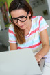 Cheerful girl with eyeglasses working on laptop