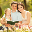 Foto: Happy mother, father and daughter read a book in the park Happy mother, father and daughter read a book in the park