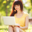 Photo: Cute woman with white laptop in the park with dandelions Cute woman with white laptop in the park with dandelions