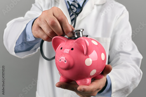Photo: Doctor holding stethoscope to piggy bank Doctor holding stethoscope to piggy bank