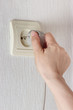 Hand inserting electric plug in the socket on the wall