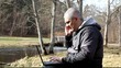 Man with cell phone, PC on a bench near river in park