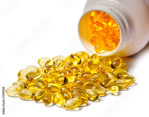 Photo: Yellow liquid capsules lie near a bottle.. Yellow liquid capsules lie near a bottle..