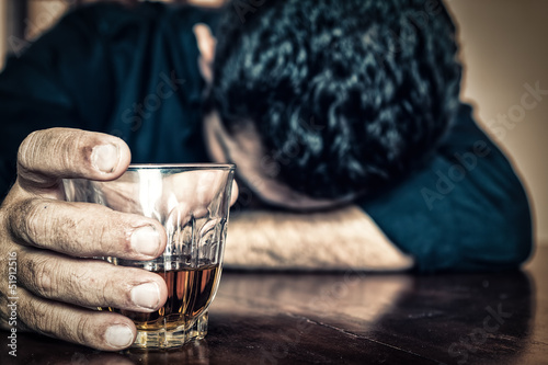 Photo: Drunk man holding a drink and sleeping on a table Drunk man holding a drink and sleeping on a table