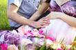 Happy pregnant couple sitting on the grass with rose petals in a