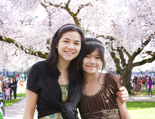 Photo: Two girls standing in front of large flowering cherry tree Two girls standing in front of large flowering cherry tree