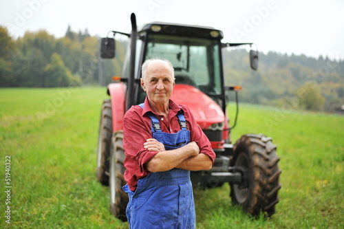 Photo: Proud farmer standing in front of his red tractor Proud farmer standing in front of his red tractor