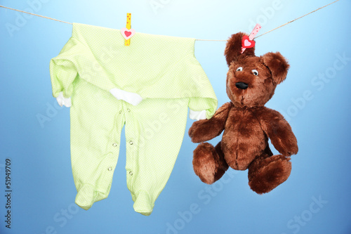 Photo: Baby clothes hanging on clothesline, on blue background Baby clothes hanging on clothesline, on blue background