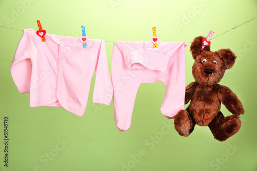 Photo: Baby clothes hanging on clothesline, on color background Baby clothes hanging on clothesline, on color background