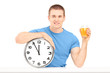 Handsome guy holding a wall clock and glass of orange juice on a
