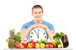 Handsome guy holding a wall clock, seated on a table full of fru