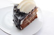 Part of a pie chocolate with nuts and prunes on a white plate.