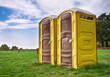 Two yellow portable toilets at a park