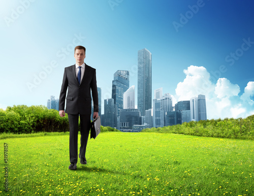 Photo: business man walking on green field and modern city business man walking on green field and modern city