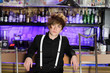 Glamorous boy in black shirt and white suspenders sits near bar