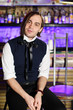 Glamorous man in  vest and white shirt sits near bar counter