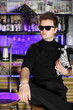 Glamorous young man in sunglasses sits near bar counter