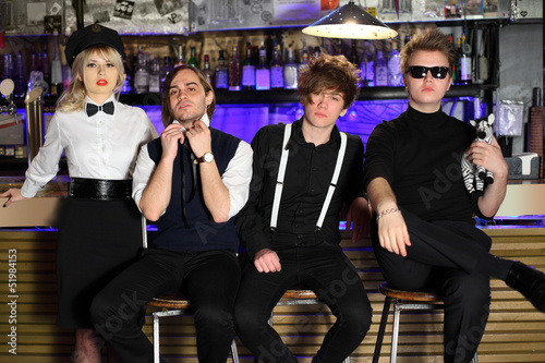 Photo: Four popular rock band in black and white pose near bar counter. Four popular rock band in black and white pose near bar counter.