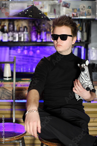 Photo: Glamorous young man in sunglasses sits near bar counter Glamorous young man in sunglasses sits near bar counter