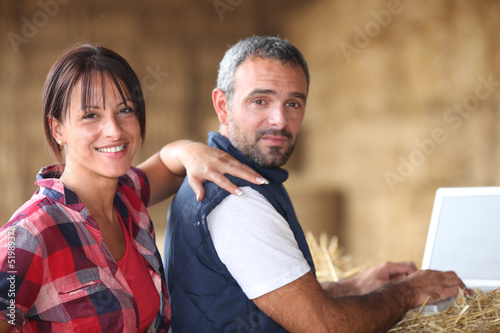 Photo: Farmer couple with laptop in barn Farmer couple with laptop in barn