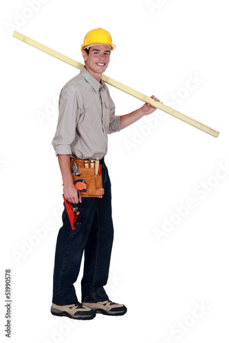 Photo: young carpenter in studio carrying plank over his shoulder young carpenter in studio carrying plank over his shoulder