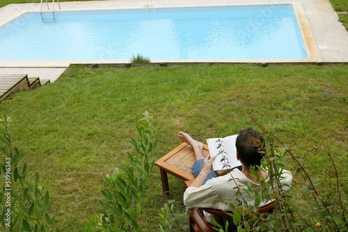Photo: Woman reading book poolside Woman reading book poolside