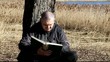 Man reading a book leaning against tree