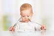baby with fork and knife eating, looking at the plate with one p