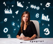 Photo: Young businesswoman sitting at desk with diagrams and statistics Young businesswoman sitting at desk with diagrams and statistics
