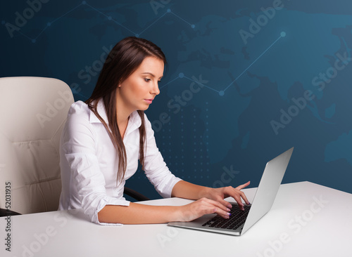 Photo: Young woman sitting at desk and typing on laptop Young woman sitting at desk and typing on laptop