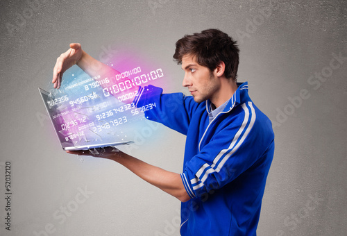 Photo: Casual man holding laptop with exploding data and numbers Casual man holding laptop with exploding data and numbers