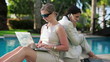 Businesswomen with laptop and cellphone by the swimming pool