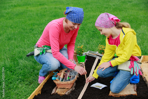 Photo: Gardening - woman with girl sowing seeds into the soil Gardening - woman with girl sowing seeds into the soil
