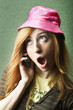 Funny young woman in pink hat gossiping on mobile