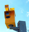 A traffic speed monitoring camera, against a bright blue sky.