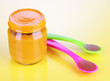 Baby food with weaning spoons on yellow background